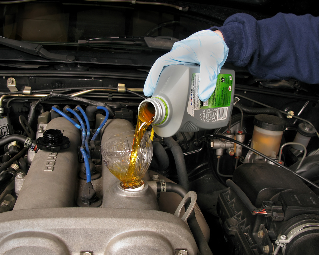 A person pouring oil to a car engine